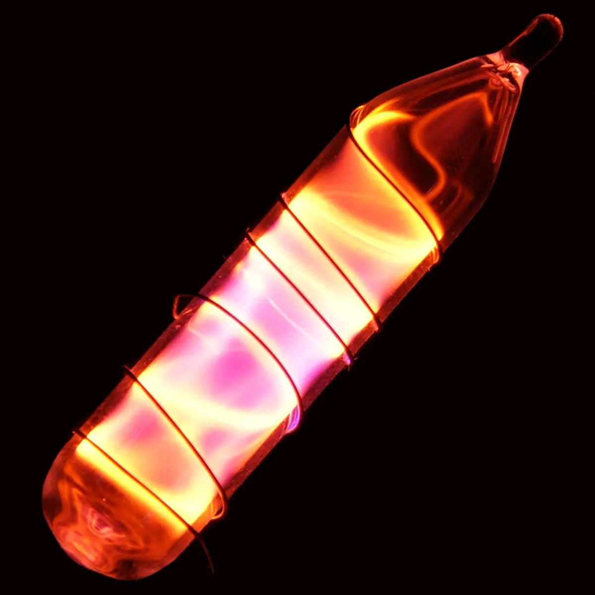 A small sealed glass vial with a wire wound round it, glowing a bright orange-red in the dark