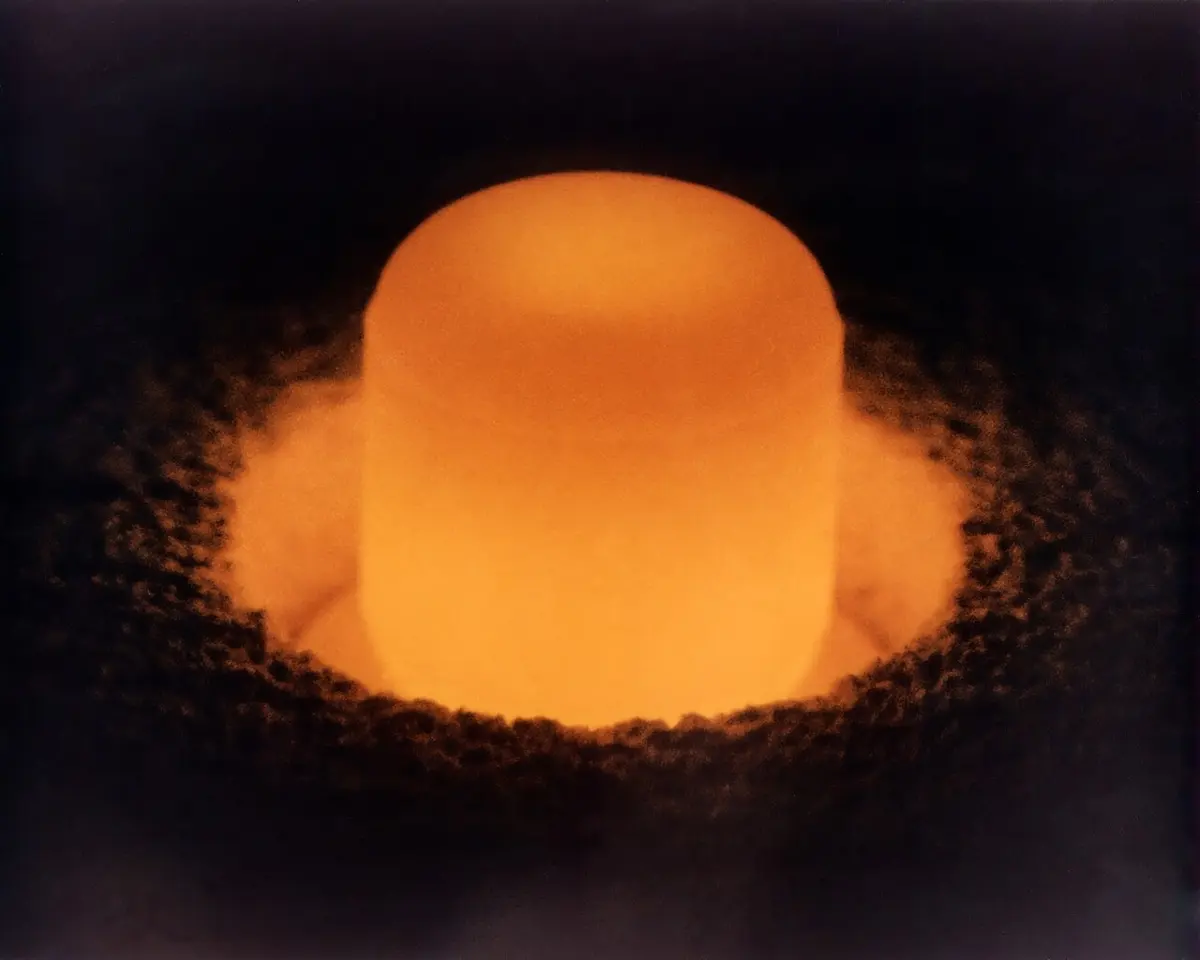 A small cylinder glowing bright orange, standing in a dark, rough bed of insulating material