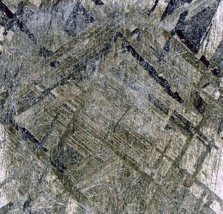 A small square of polished gray metal covered with a criss-cross pattern of straight bands at different angles