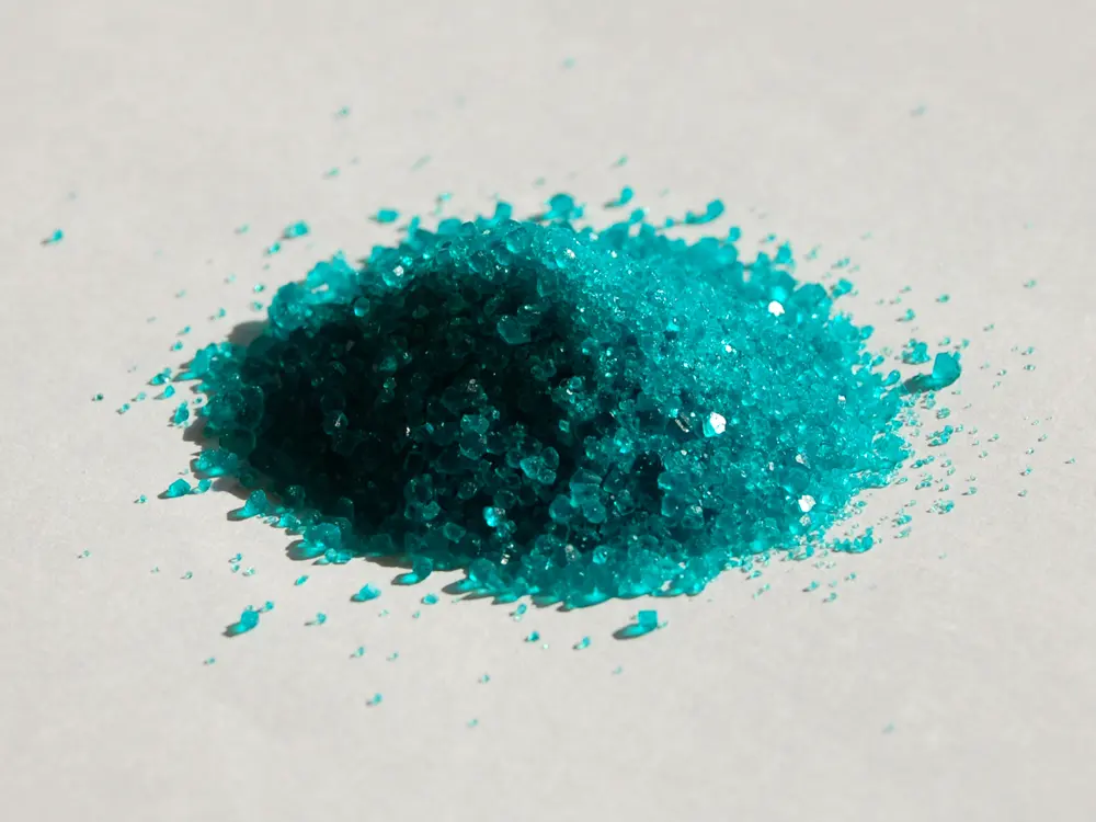 A small heap of glassy, blue-green crystals on a white surface