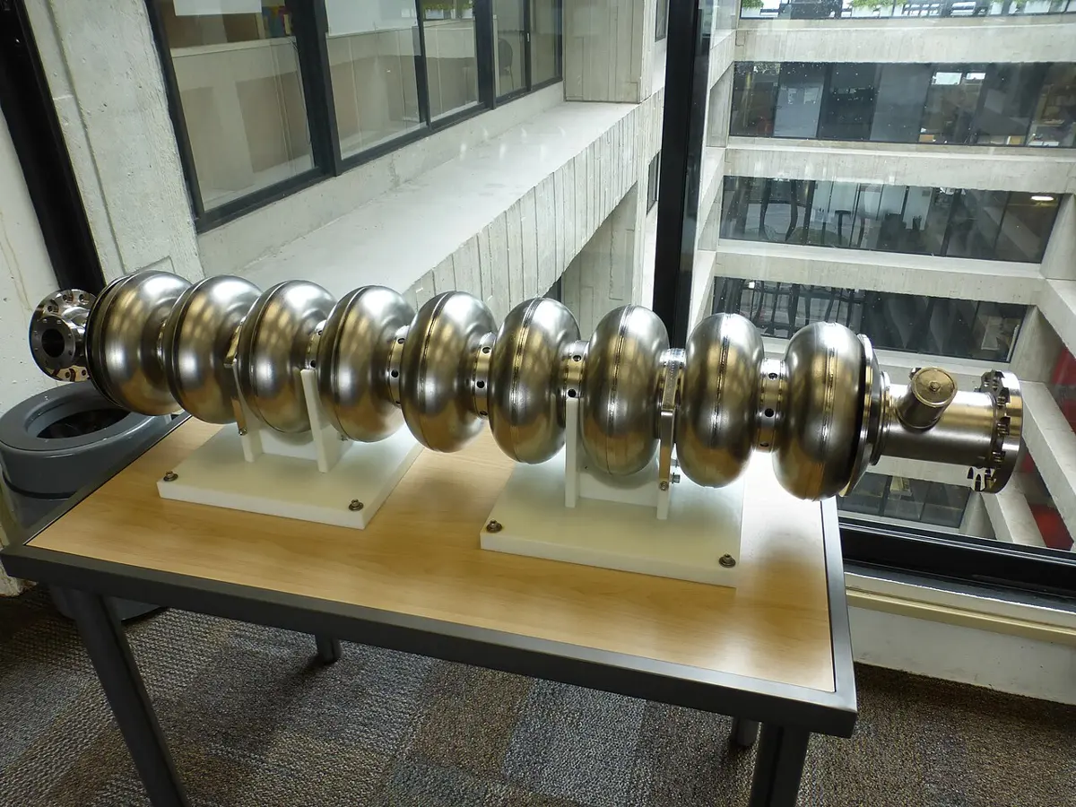 A shiny metal tube made of nine round bulges in a row, like a string of beads, resting on two stands on a table