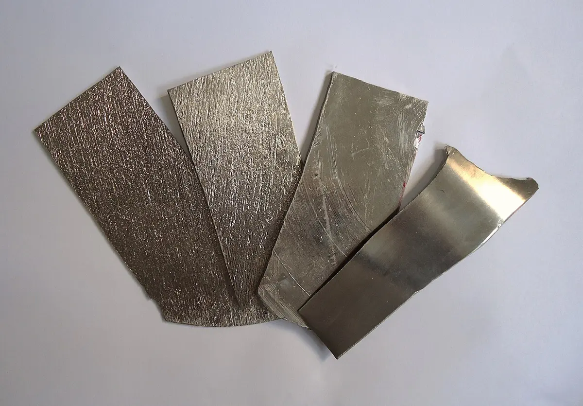 Four flat strips of gray metal fanned out on a white surface, some with a rough, scratched surface and one smooth and shiny
