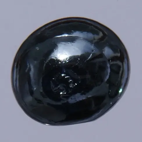 A rounded, glossy bead of very dark, bluish-gray metal, shining like wet glass