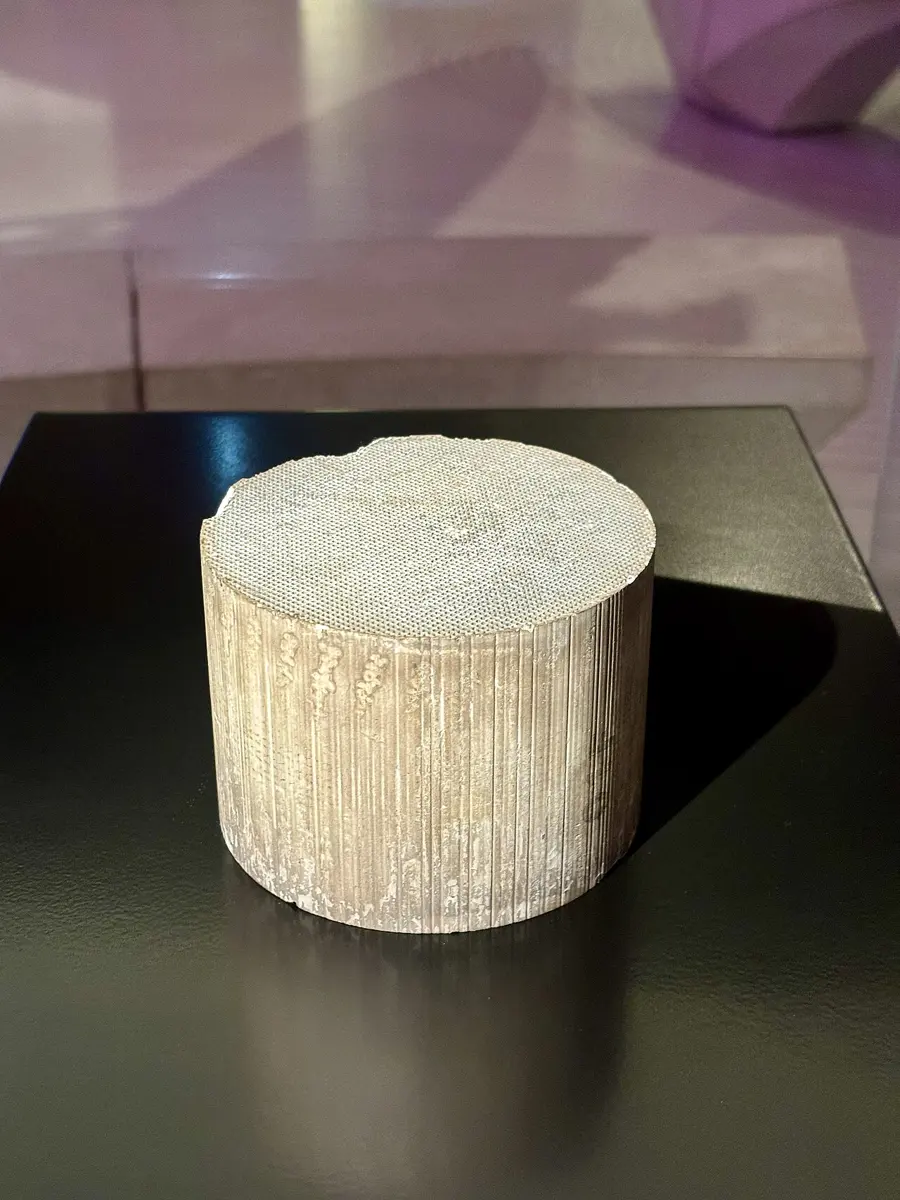 A short, pale gray ceramic cylinder standing on a black base; its flat top is covered in a fine grid of tiny square holes