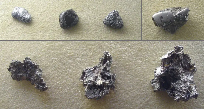 Six gray metal nuggets on a beige cloth, some smooth and rounded, three rough and spongy with many holes