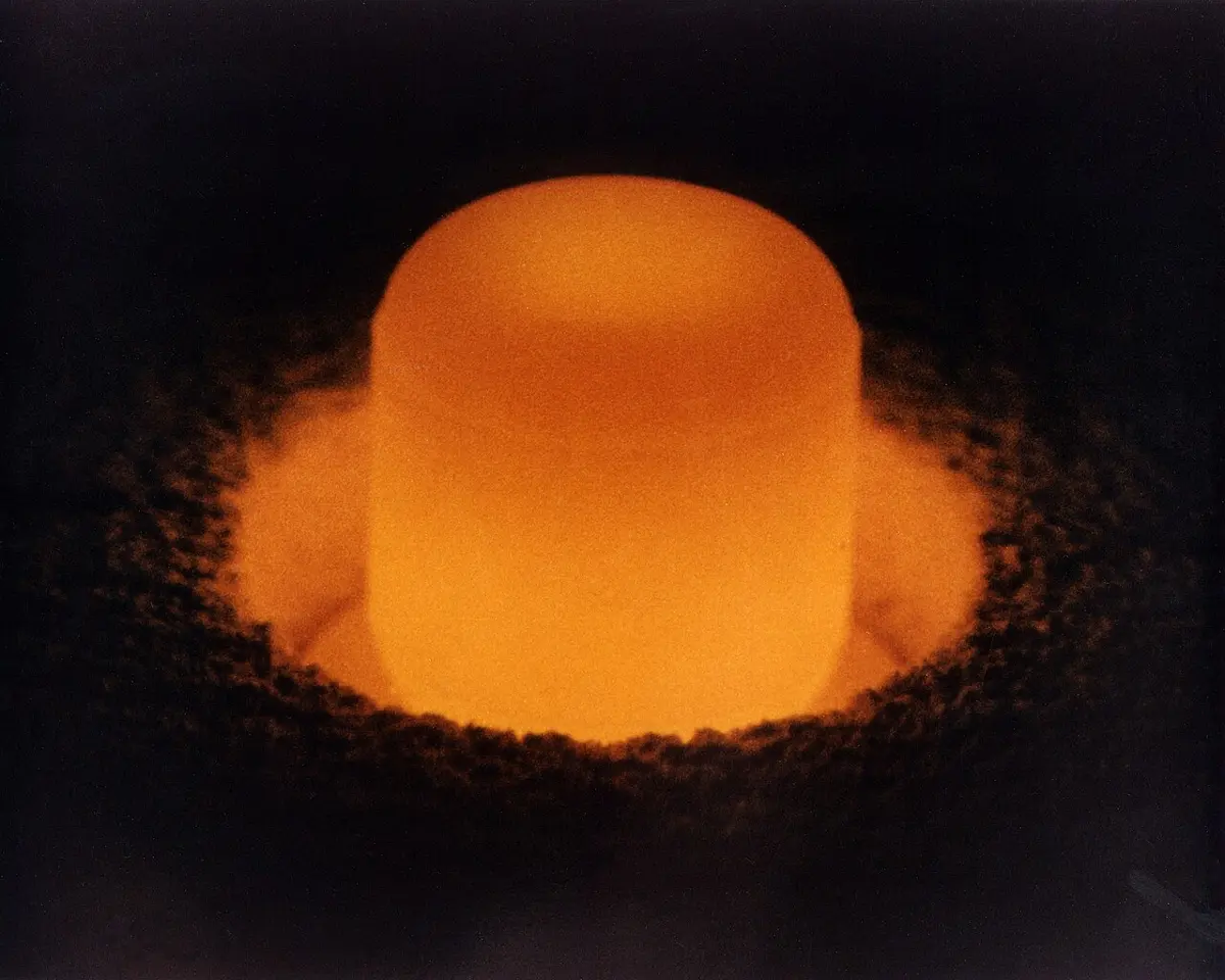 A small cylinder glowing bright orange in the dark, standing in a bed of dark granules lit orange by its glow