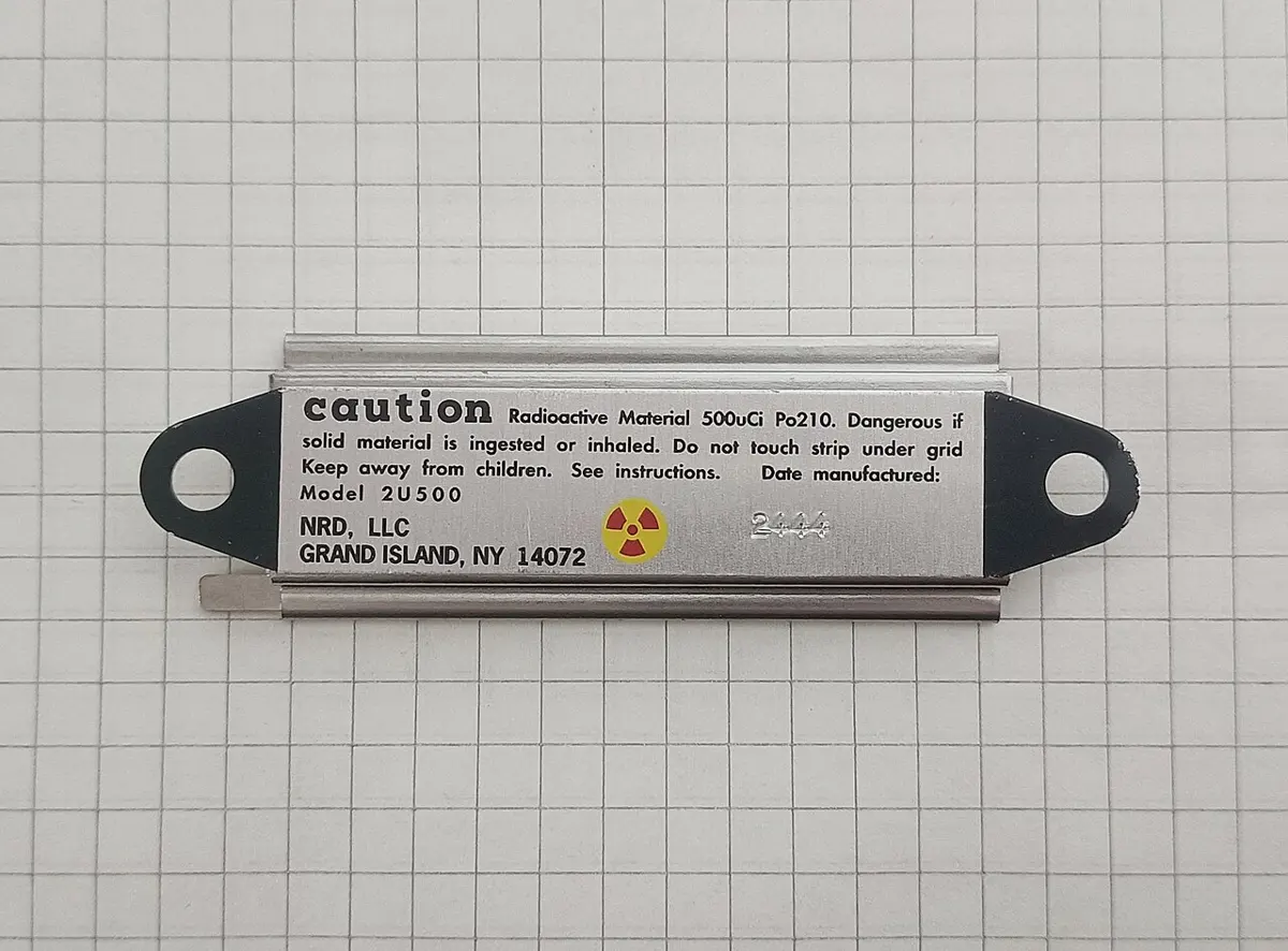 A narrow metal bar on squared paper with a hole at each end and a printed caution label with the radiation symbol