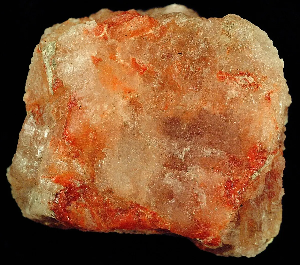 A lump of rock made of pale, glassy salt crystals streaked with orange-red