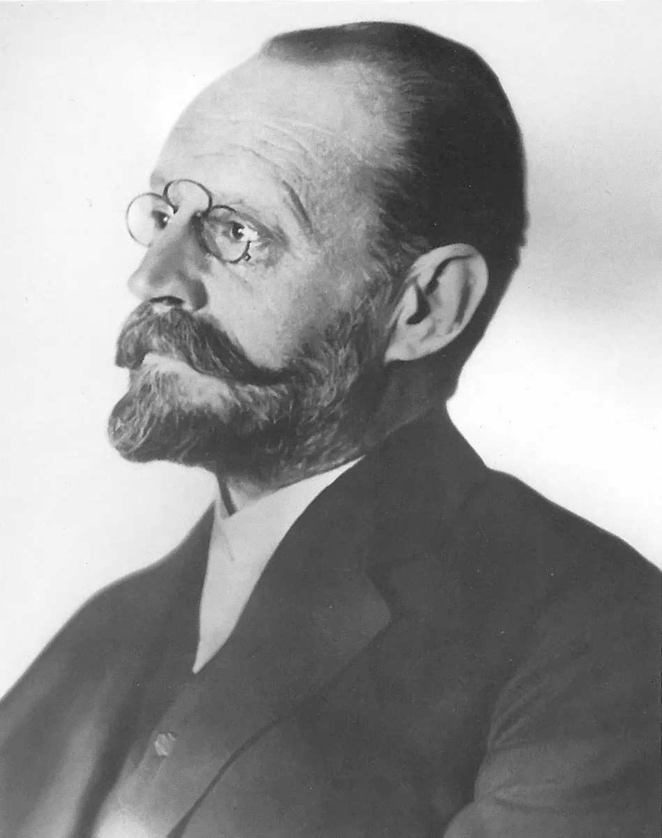 Black-and-white photo of a balding man with a beard and round pince-nez glasses, in a dark suit, looking to the left
