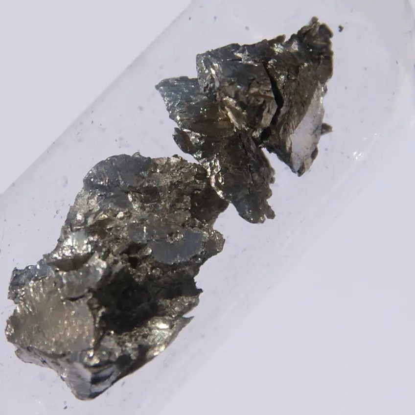 Two rough, crumbly lumps of gray metal with a faint bronze sheen, in a clear glass tube