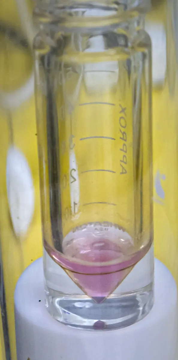 A small glass vial with a little pale pink liquid in the bottom, held upright