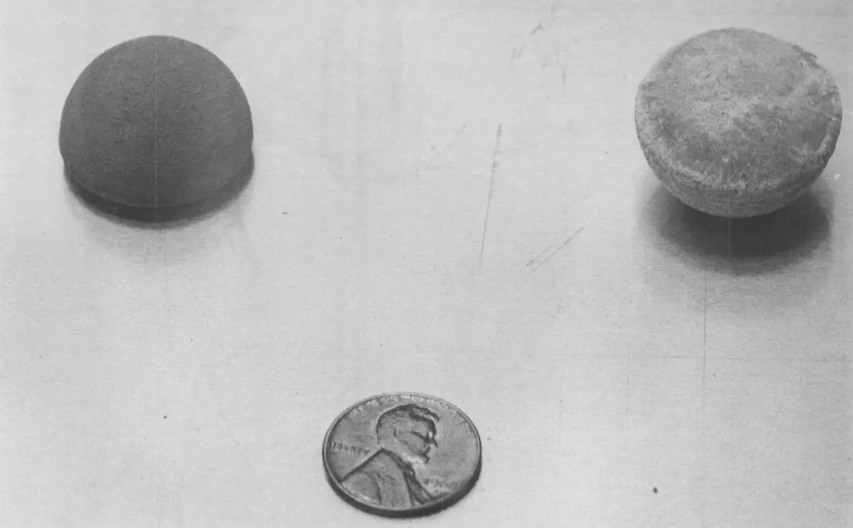 Black-and-white photo of two small round buttons of metal, one dark and one pale, with a US one-cent coin below them