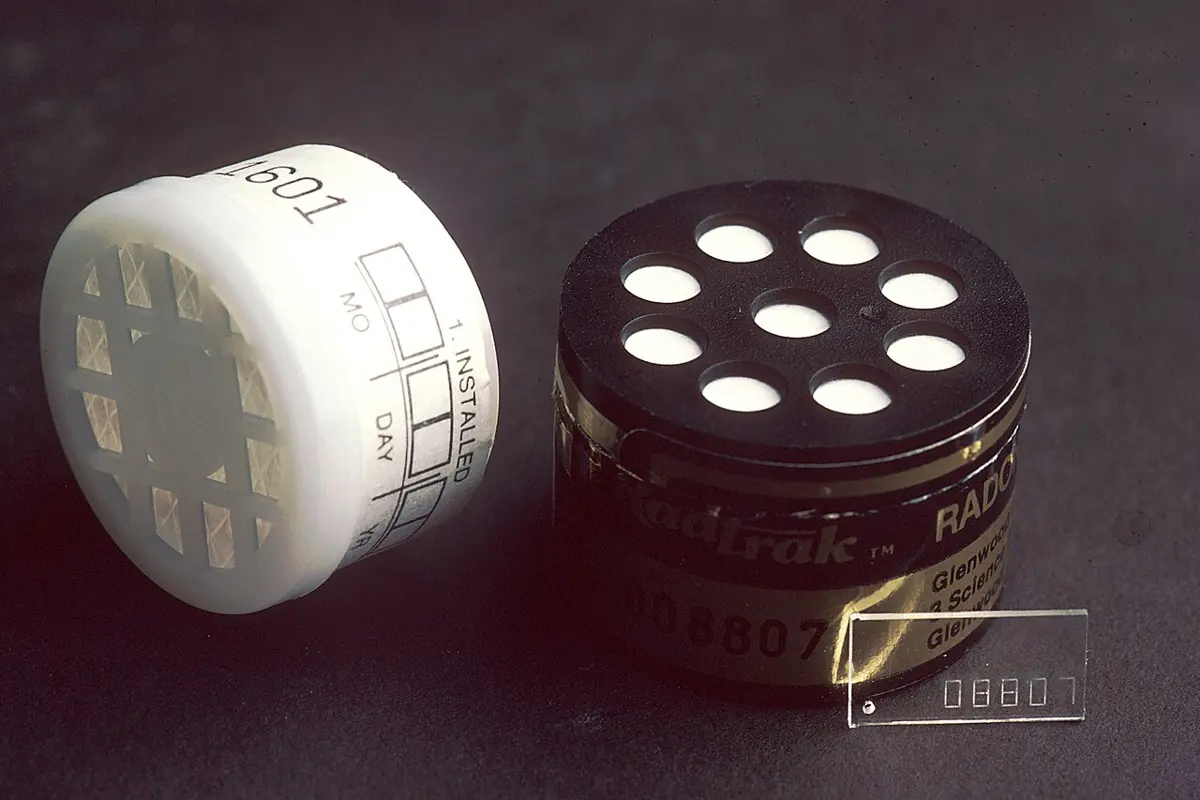 Two small round plastic containers: a white one with a grid on top and a label with spaces for a date, and a black one with eight round holes in its lid