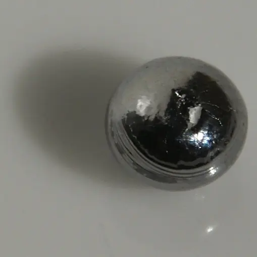 A small, round, mirror-bright bead of silvery-gray metal on a white surface, reflecting the room around it