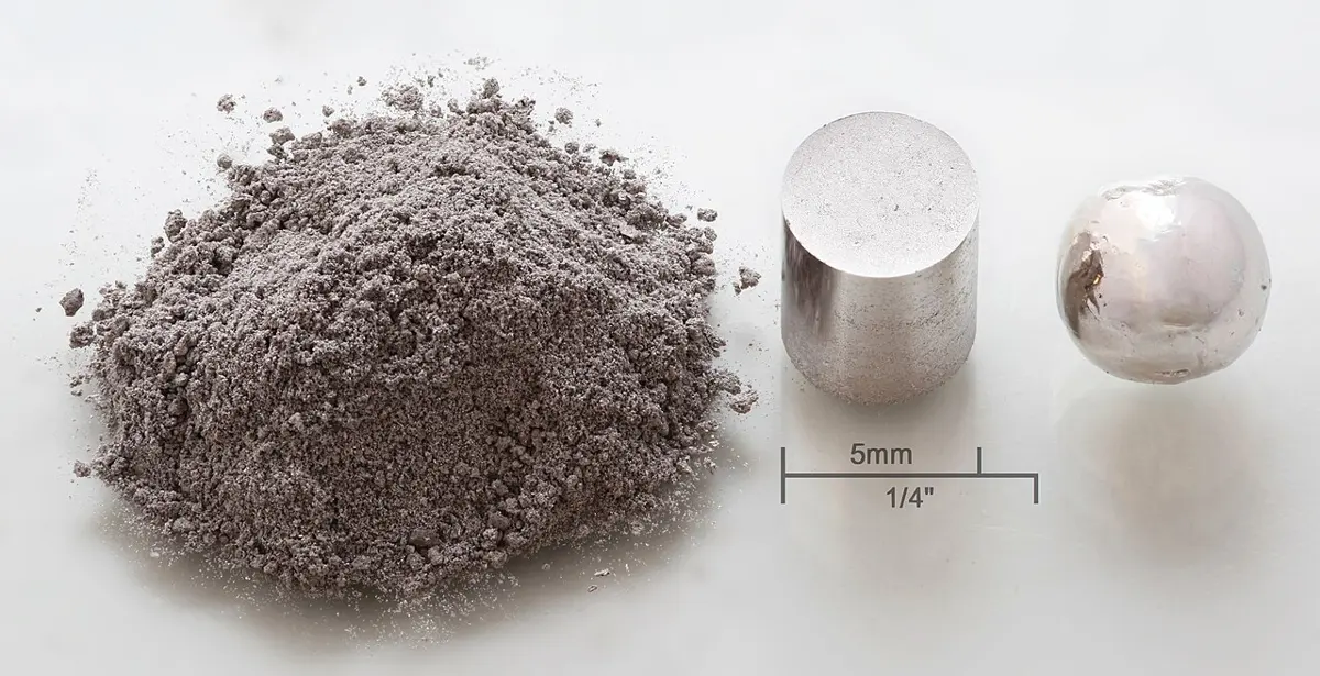 A heap of gray powder, a small shiny metal cylinder and a bright silvery bead side by side, with a 5 mm scale bar
