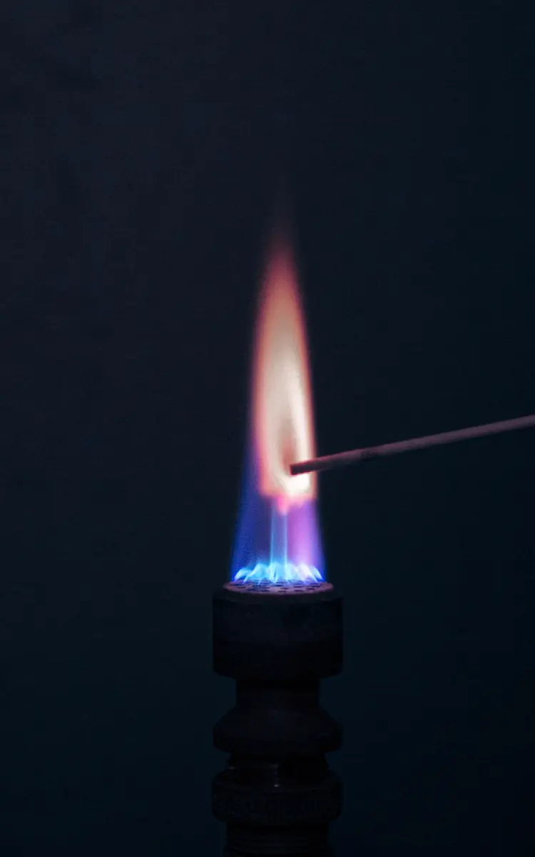 A small gas flame against a dark background: blue at the bottom, and a tall pinkish-red flame above, where a thin wire holds a rubidium salt in it