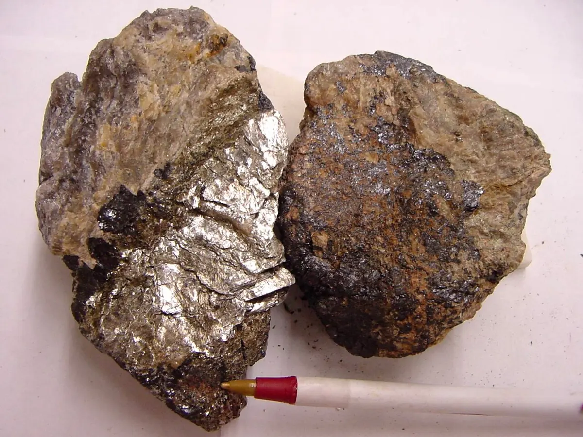 Two brownish lumps of rock with dark, shiny patches, beside the tip of a pen