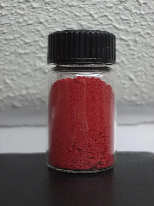 A small glass jar with a black screw lid, filled with a dark red powder