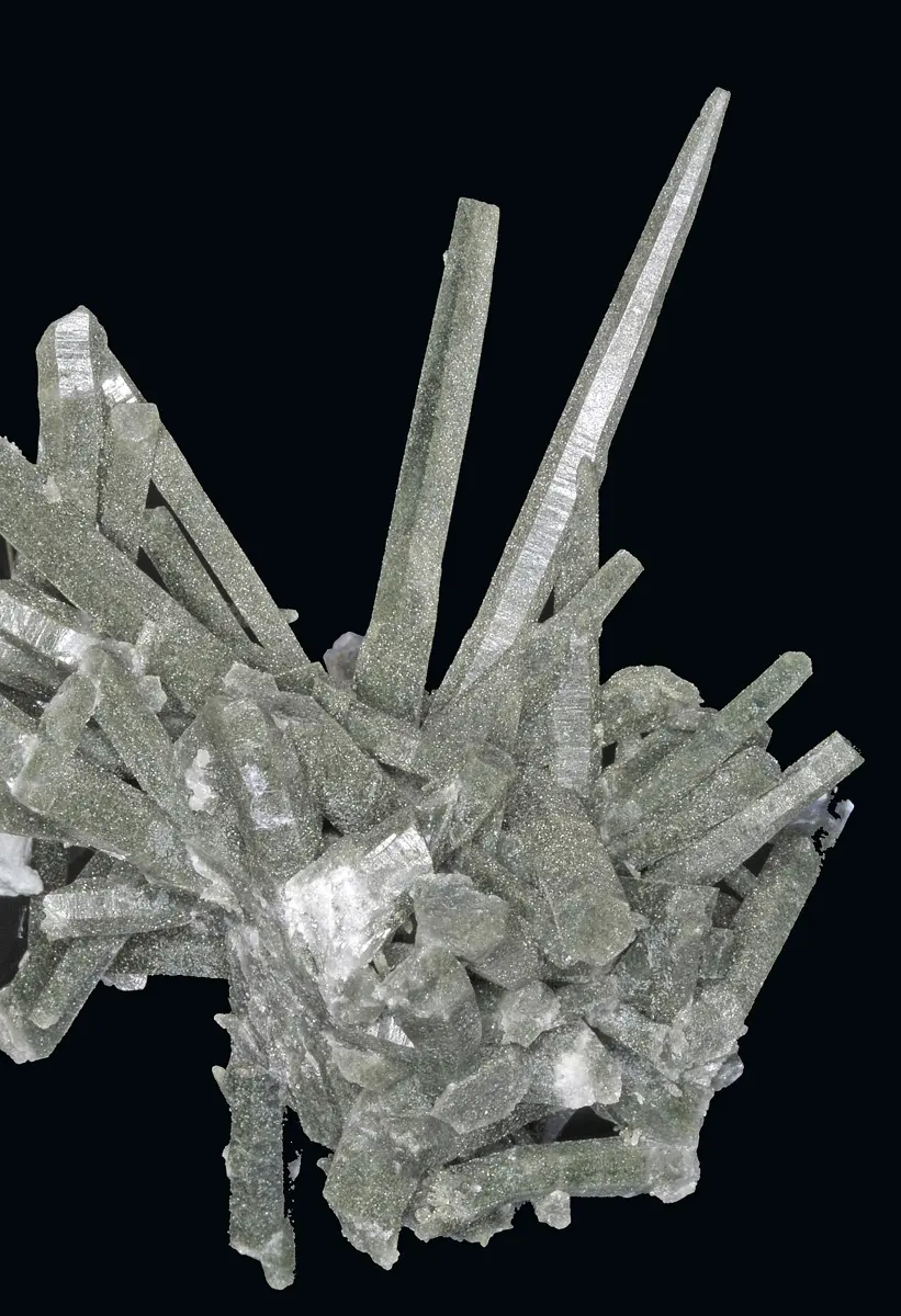 A spray of long, six-sided, pale green crystals pointing in all directions, on a black background