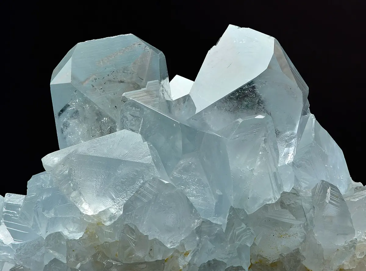 A cluster of large, clear, pale blue crystals with flat faces and sharp edges, on a black background
