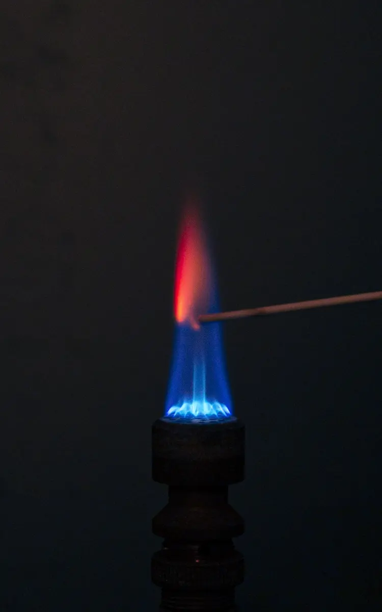 A blue gas flame in the dark with a thin rod held in it; above the rod the flame burns bright red