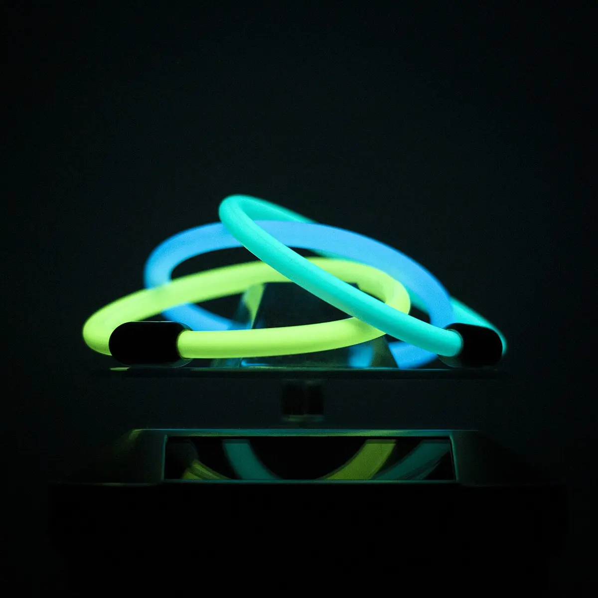 Three glowing bracelets, two pale blue and one yellow-green, lying in the dark