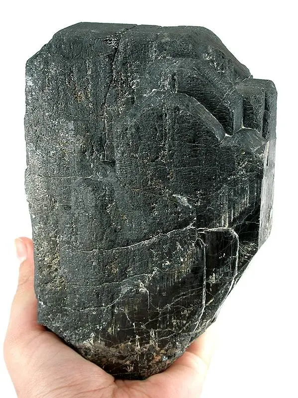 A hand holding a single huge, dark gray to black crystal with flat faces and stepped edges, bigger than the palm