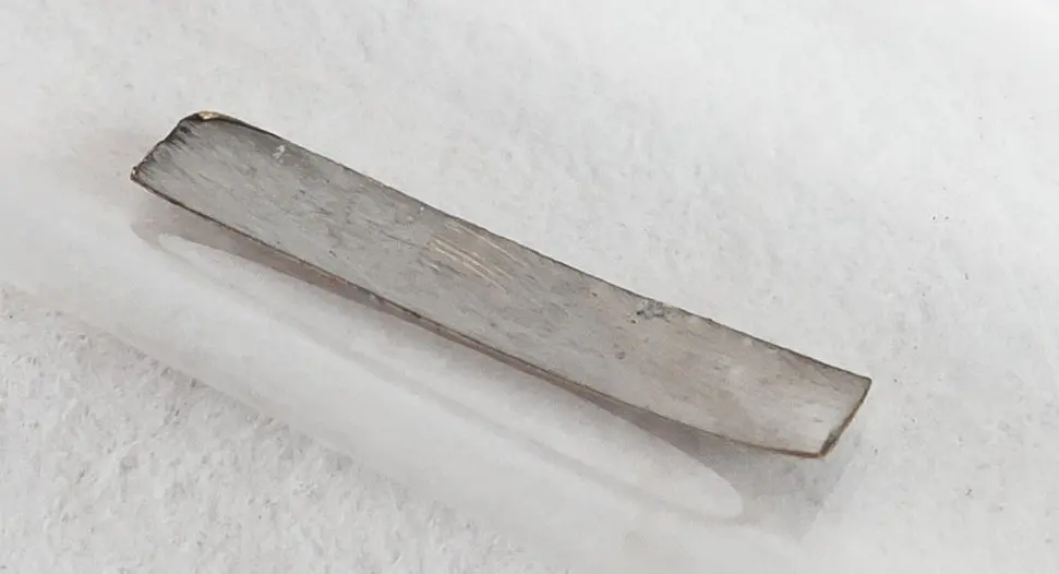 A thin, flat strip of gray metal inside a clear glass tube, lying on a white cloth