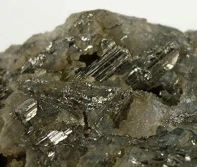 A rough rock with shiny, silvery, finely striped crystals among dull pale gray ones