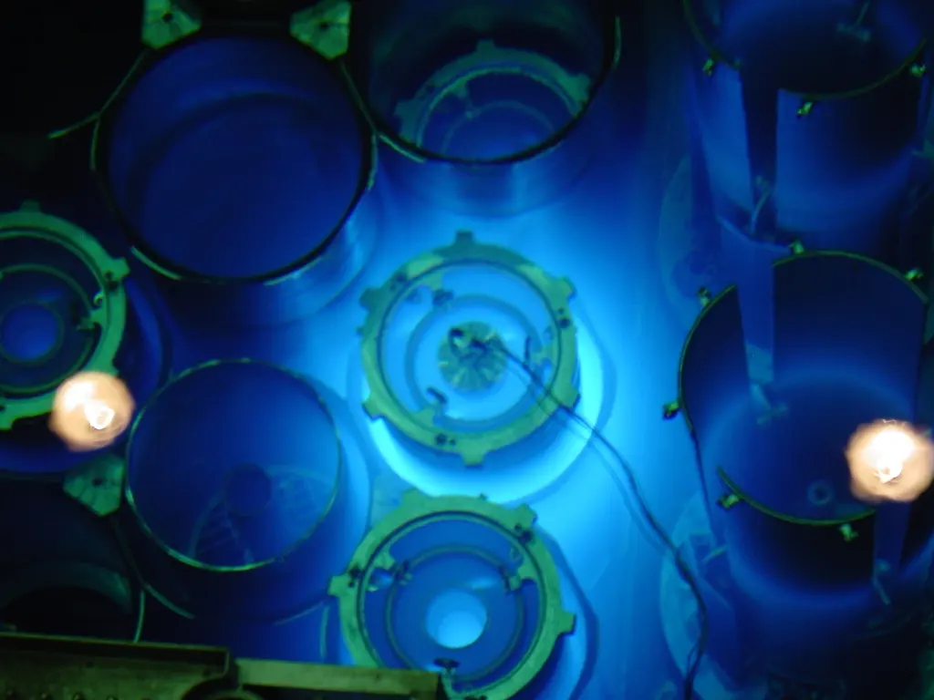 Looking down into a deep pool of water: round metal structures glow bright blue under the water, with two small lamps shining