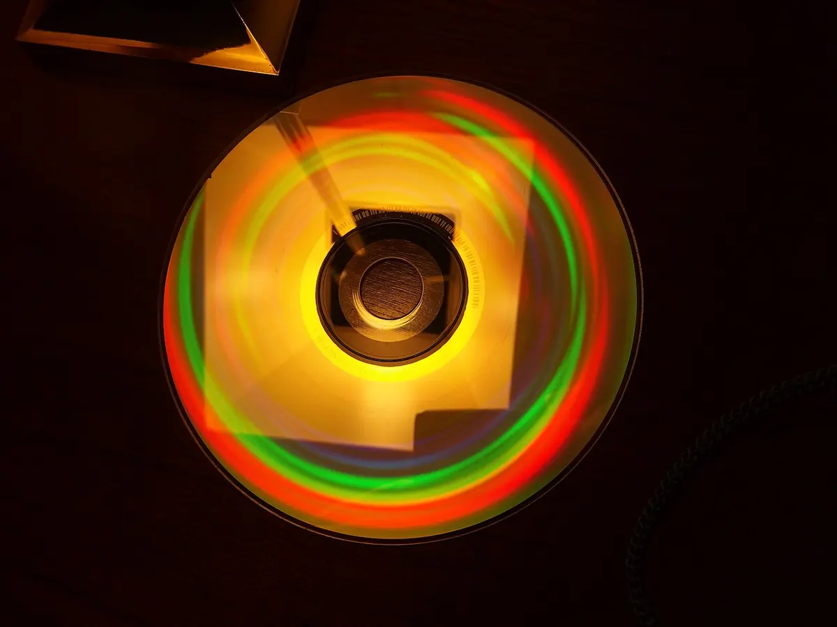A DVD lying under a lamp; around its center hole the reflected light forms rings of separate colors: red, yellow-orange, green and a little blue
