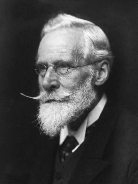 A black and white photograph of an elderly man with round glasses, white hair, a white beard and a long mustache, in a dark coat
