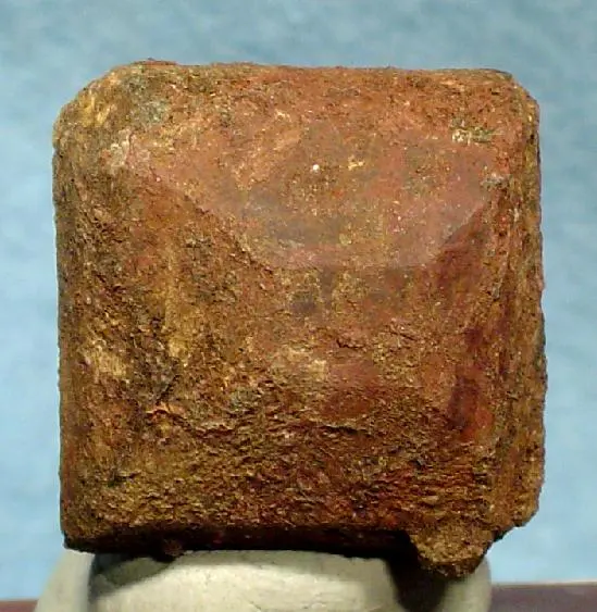 A single rough, rust-brown crystal shaped like a square block with a low pointed top, standing on a small gray stand