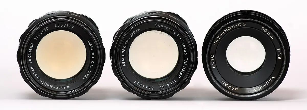 Three black camera lenses seen from the front: the glass of the two on the left is tinted yellow, the one on the right is clear