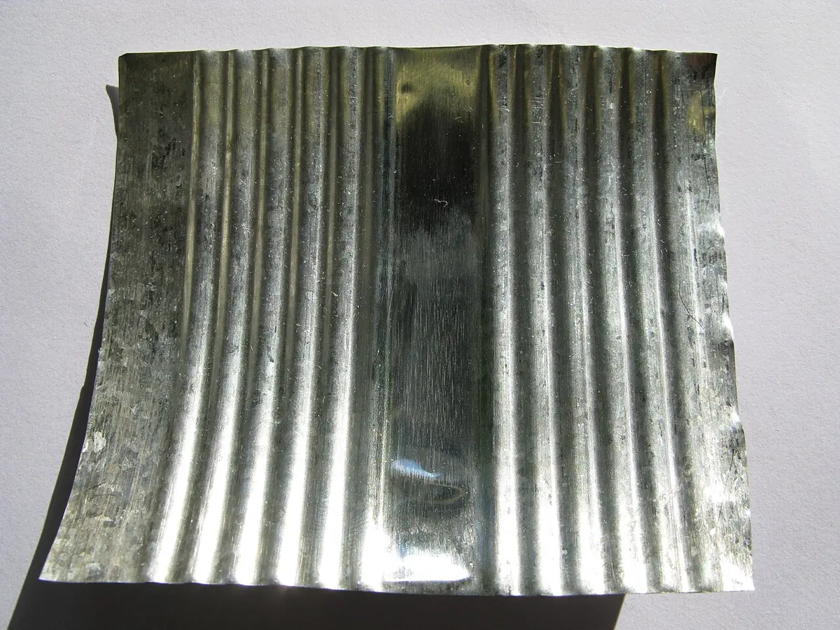 A curved, ribbed sheet of bright silvery metal, cut from the side of a can, on a white background
