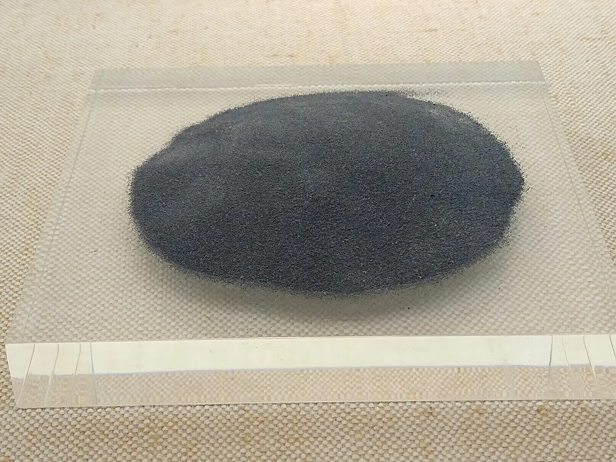 A round heap of fine dark gray sand spread on a sheet of glass