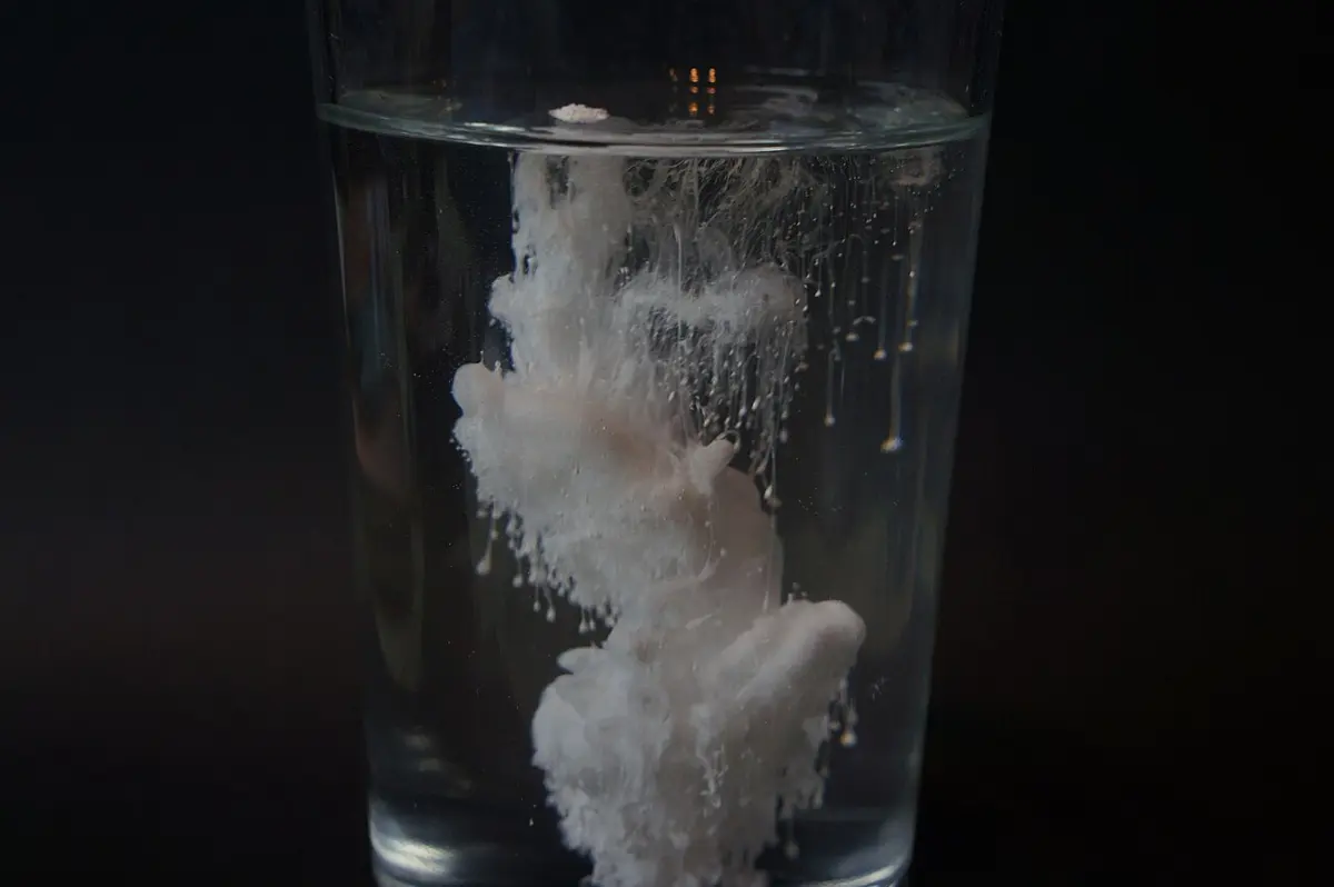A glass of clear water against a black background, with a thick white cloud of powder sinking through it in swirls