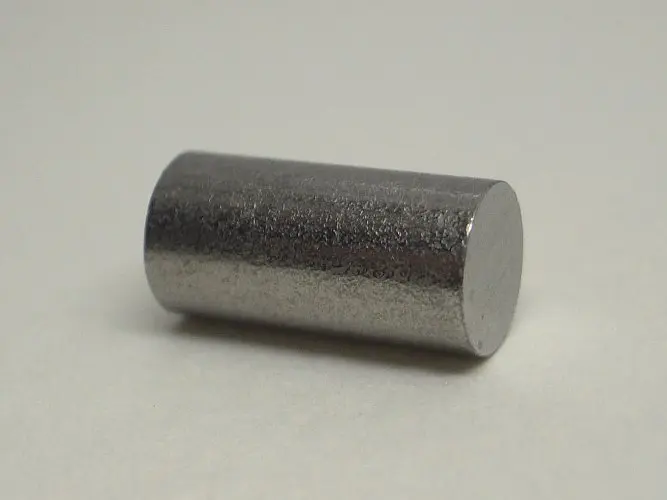 A short, solid cylinder of gray metal with a slightly rough, shiny surface, lying on a white table