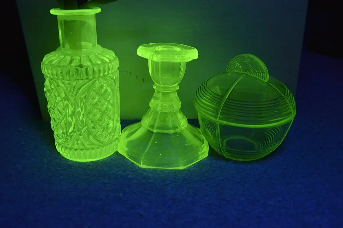 A cut-glass bottle, a candlestick and a covered dish, all glowing bright green against a dark blue background