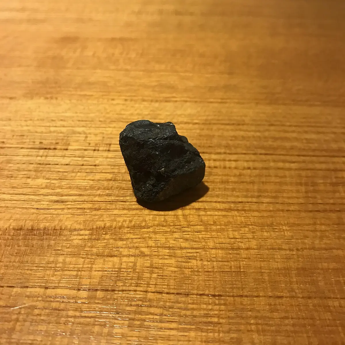 A small, rough black lump of rock on a wooden surface