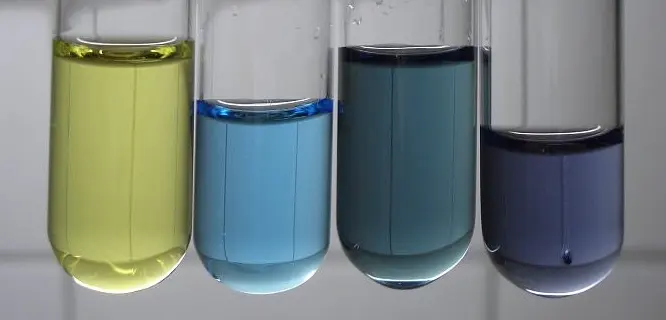 Four test tubes in a row holding colored solutions: yellow, light blue, dark blue-green and violet
