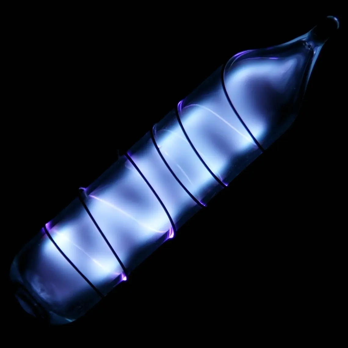 A small sealed glass vial glowing pale blue and violet in the dark, with a wire coiled round it