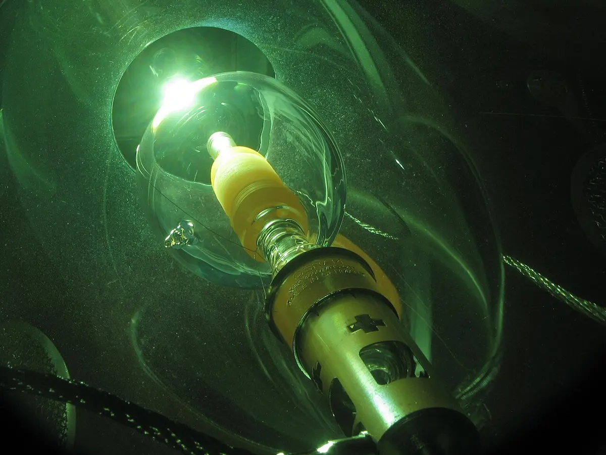 A glass bulb on a metal base, seen through a green filter, with a dazzling white spot of light inside it