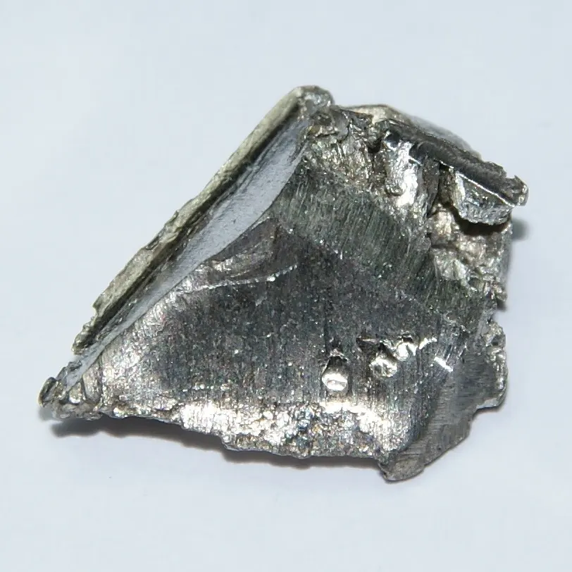 A small, rough lump of silvery-gray metal, with one smooth, finely scratched face, on a white background