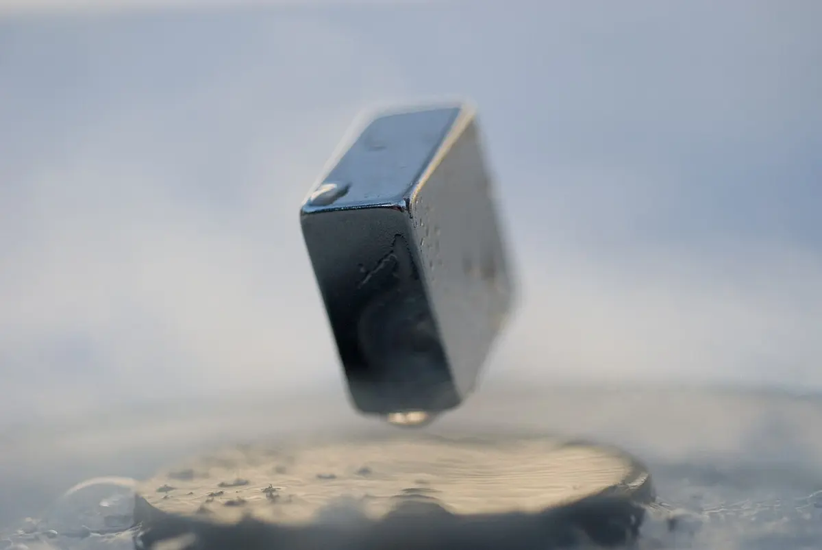 A small dark rectangular magnet floating in the air above a round gray disc, with cold mist around the disc