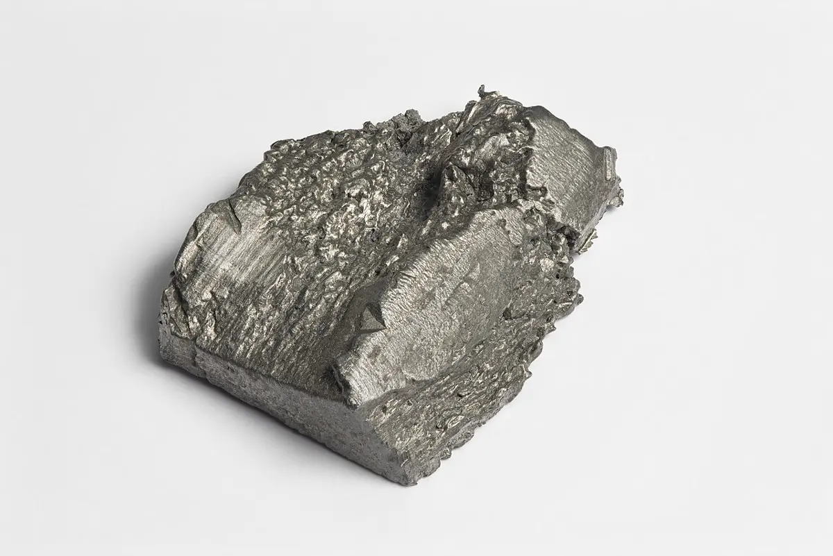 A gray metal lump with one smooth, flat cut face and one rough, crystalline face, on a white background