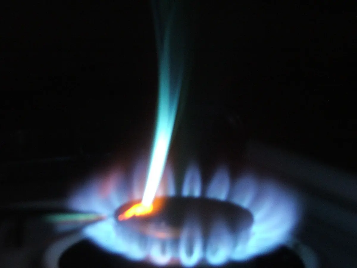 A gas stove flame, blue at the base, with a bright streak of bluish-green and orange flame rising from a small piece of metal held in it