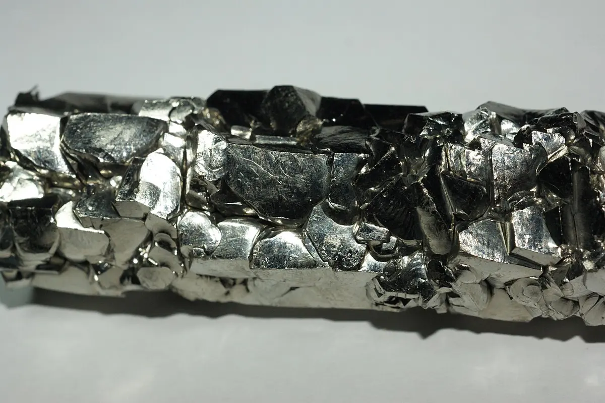 A bar of bright, silvery metal built of many shiny, flat-faced crystals packed together