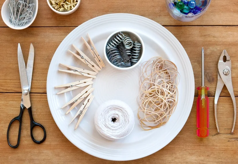 A plate of springs, clothespins, rubber bands, and string beside scissors, pliers, and a screwdriver