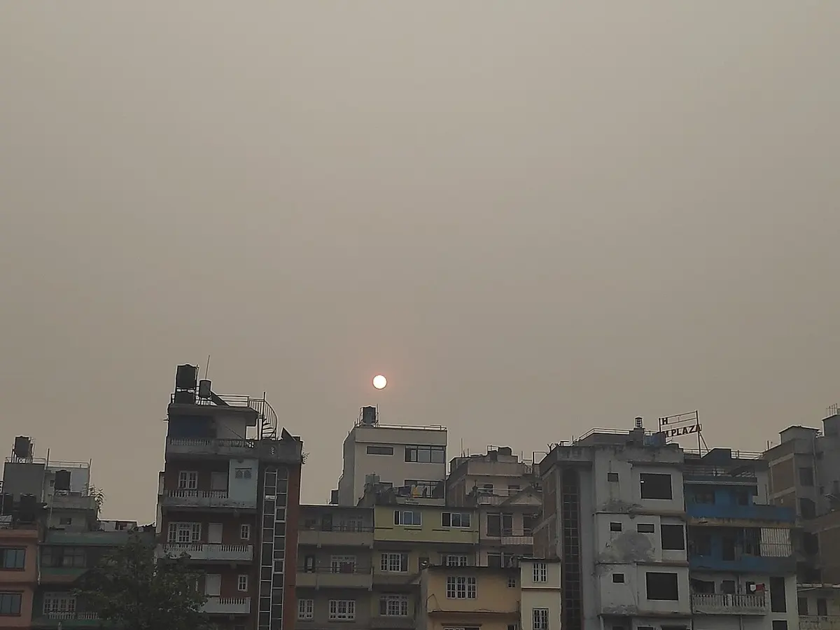 A row of concrete houses under a flat gray-brown sky, with the Sun a small, pale disc in the haze above them